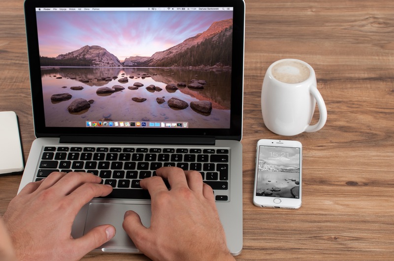 Apple computer on desk with mug and phone
