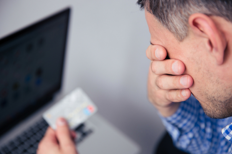 Man upset holding a credit card by computer