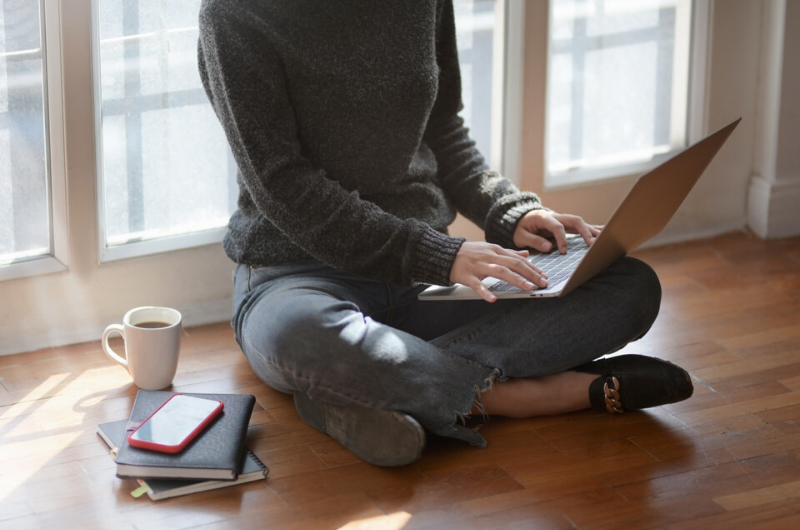 Woman in gray sweater by window using a laptop