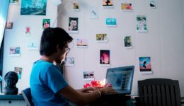 Man in blue shirt on a laptop in a room with photos taped to wall