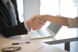 Person in black suite shaking hands with another person over a laptop